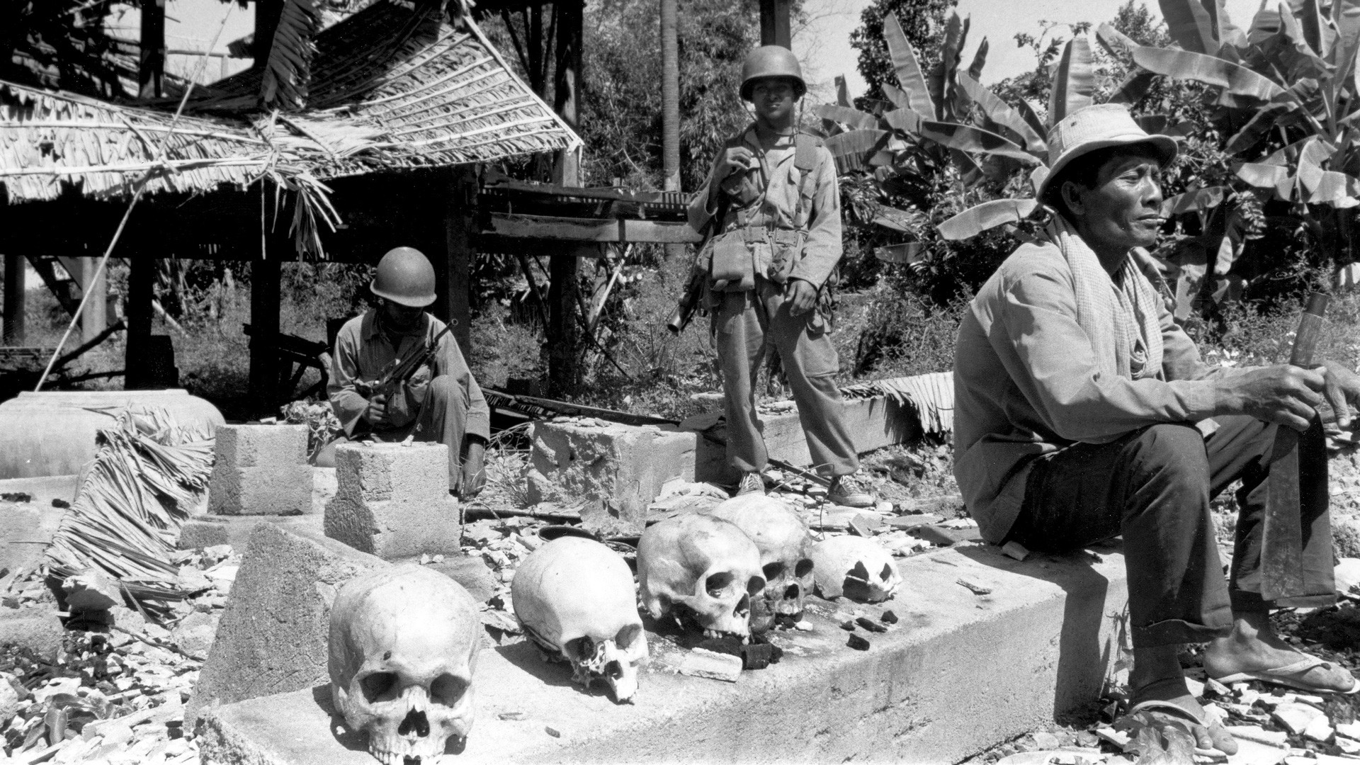 Камбоджийские сельские жители сидят возле человеческих черепов, найденных после того, как правительственные войска отвоевали деревню около Пномпеня. Это останки жителей и солдат, убитых повстанцами-кхмерами, которые захватили город во время боёв. Фото © AP Photo