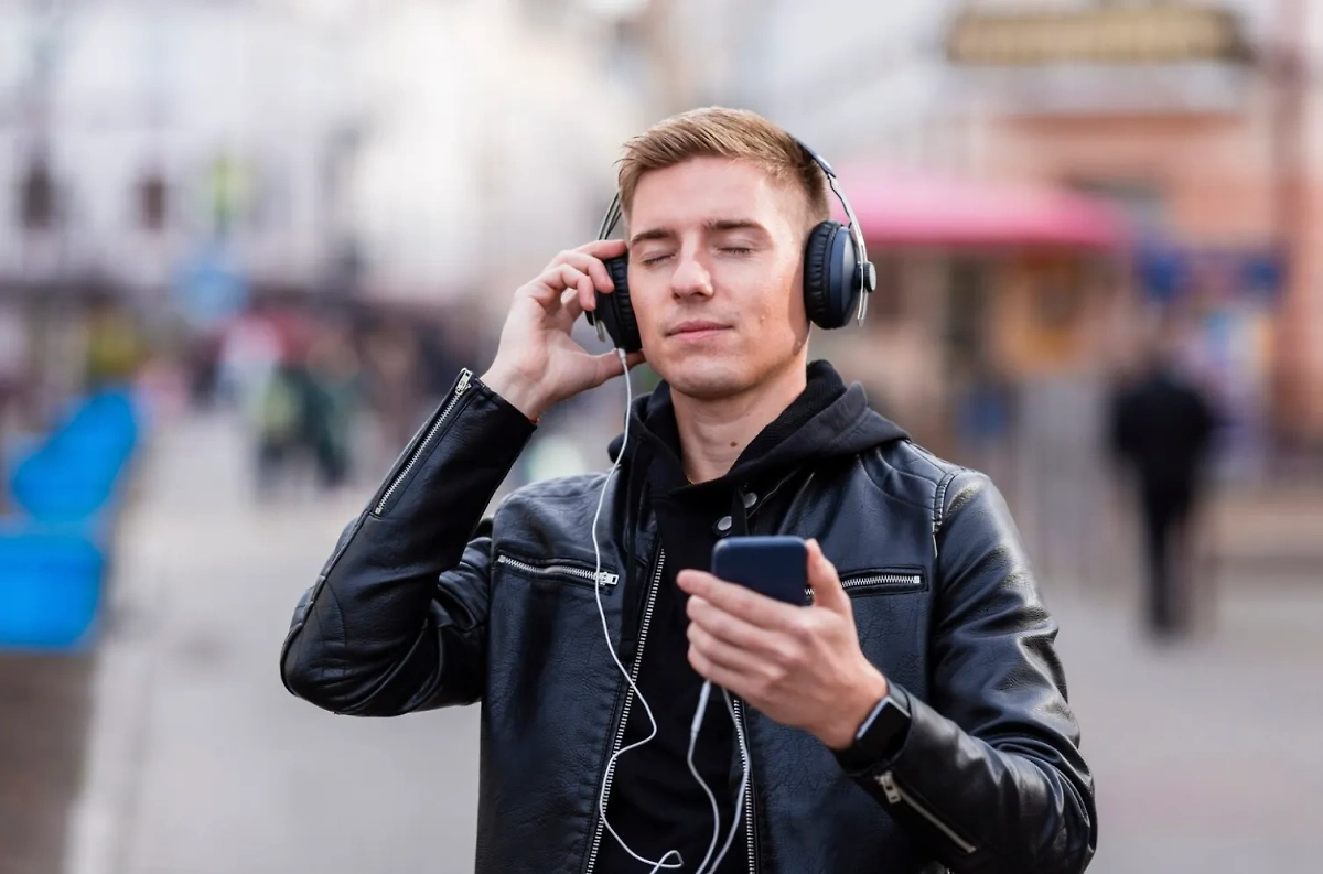 Молодой человек слушает любимые песни в наушниках на полной громкости, не представляя, что это может привести к тугоухости. Обложка © Freepik