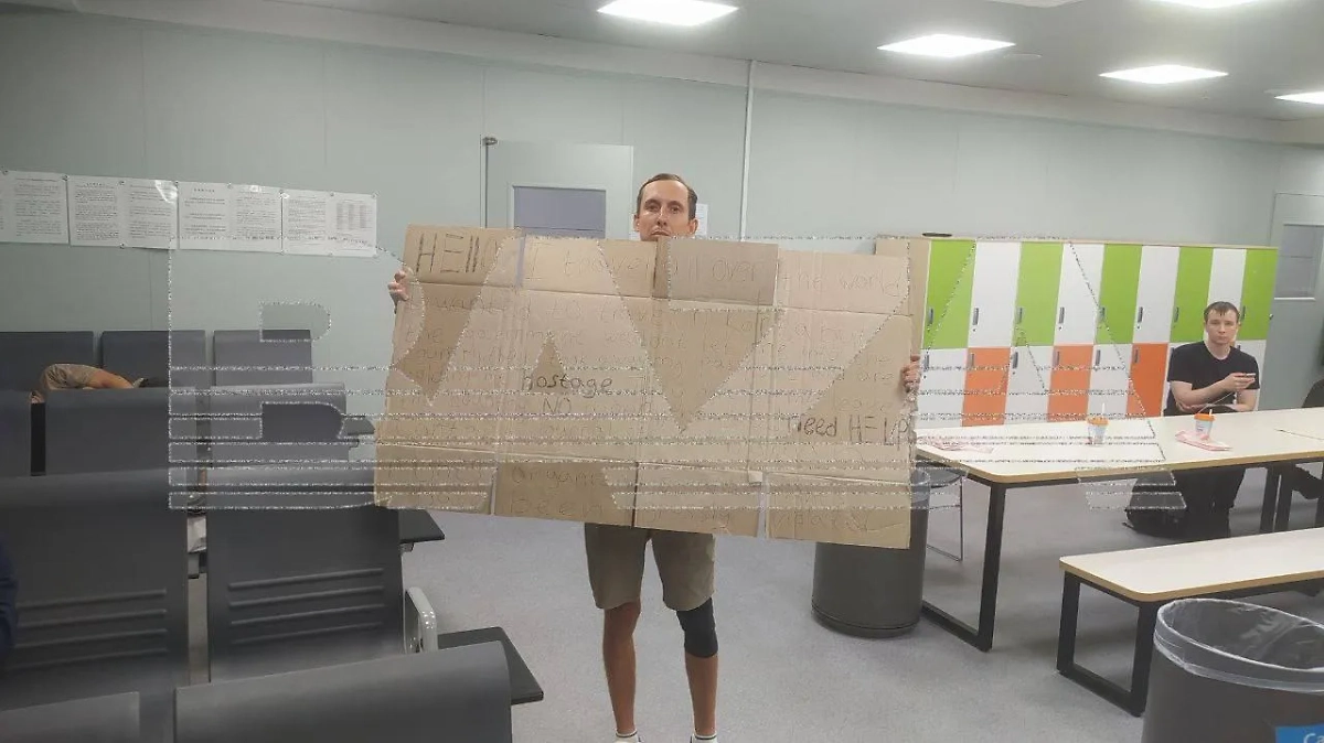 Андрей написал на картонке, что его удерживают против воли, чтобы улететь из Южной Кореи. Фото © Telegram / Baza