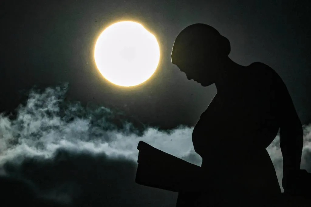 Частичное солнечное затмение на фоне скульптуры «Девушка с книгой» на крыше Российской государственной библиотеки в Москве. Обложка © ТАСС / Евгений Мессман