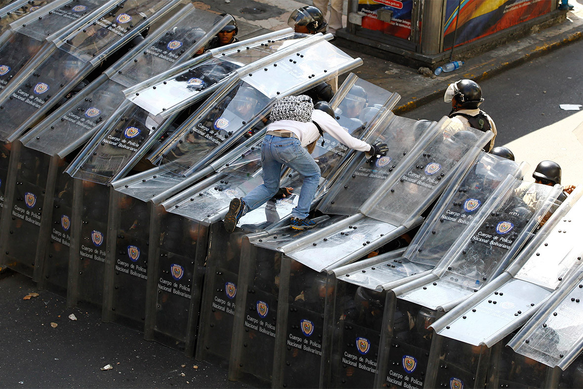 Демонстрант&nbsp;запрыгивает на стену из полицейских щитов во время акции протеста в Каракасе
Фото: &copy; REUTERS/David Mercado