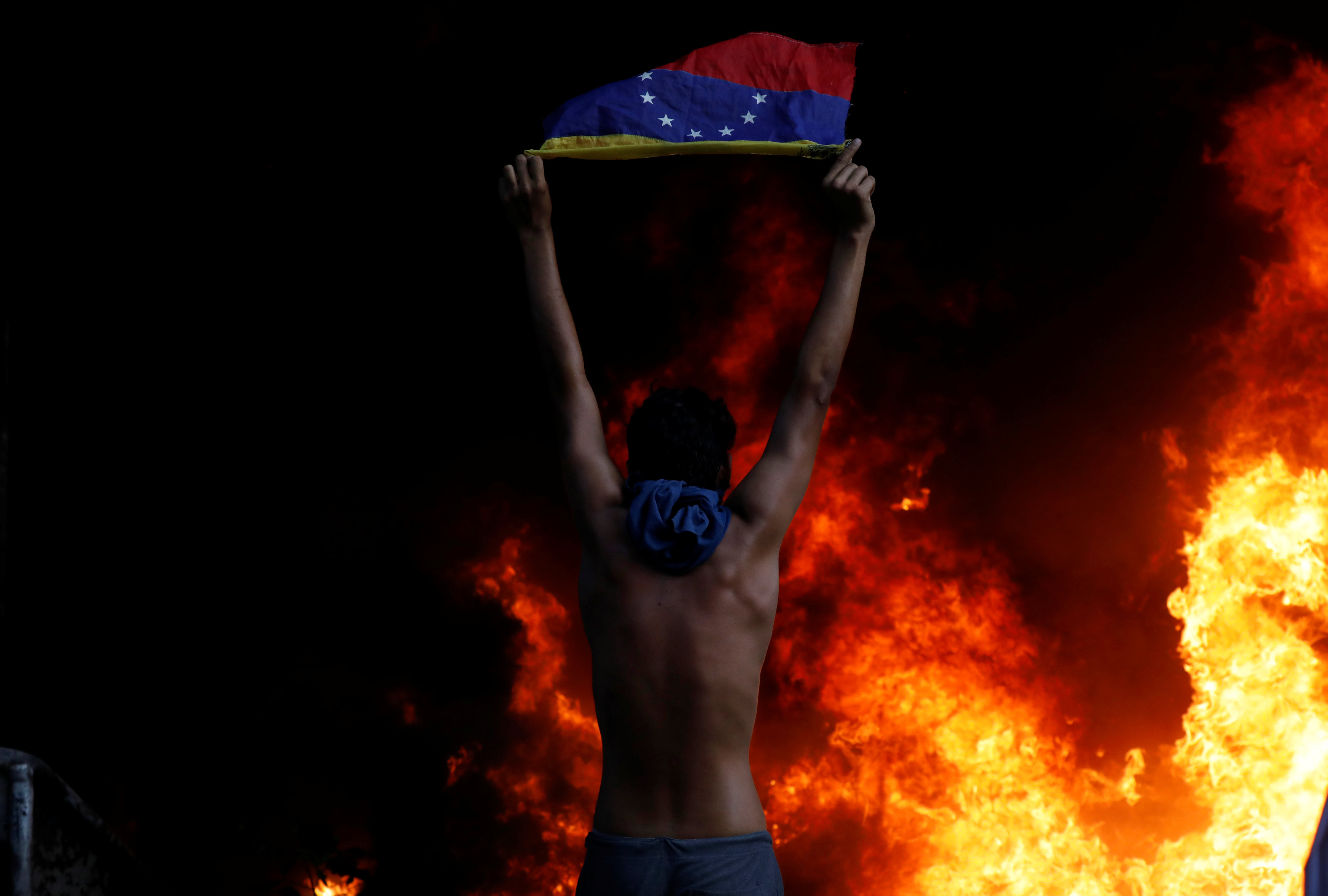 Протестующий&nbsp;держит национальный флаг, стоя перед горящим зданием Верховного суда Венесуэлы. Фото: &copy; REUTERS/Carlos Garcia Rawlins