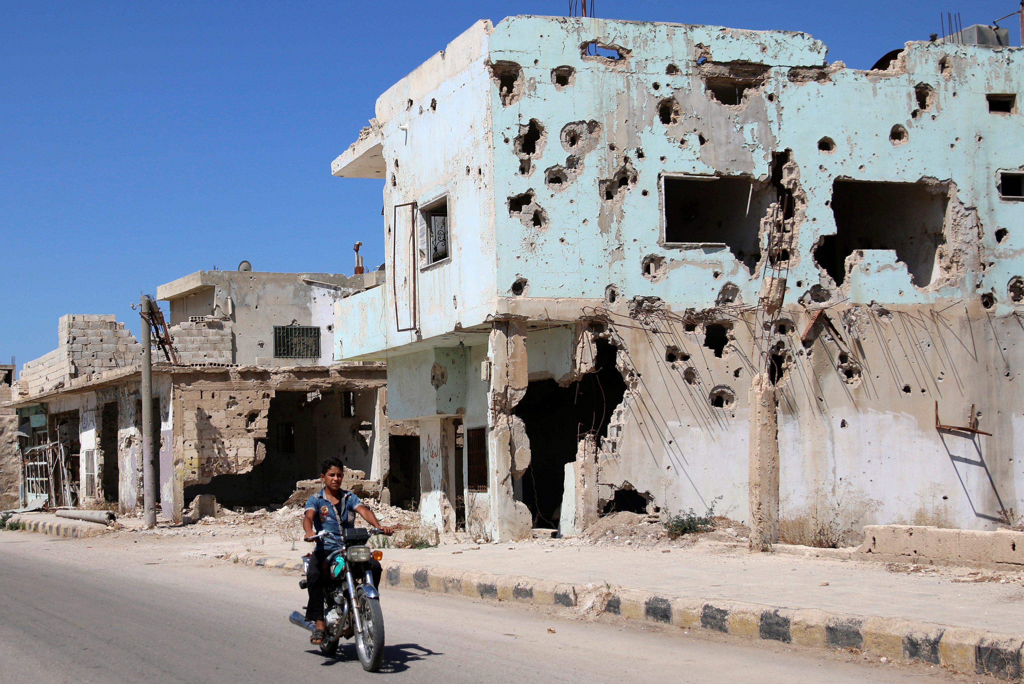 Юноша на мотоцикле на фоне повреждённого здания в сирийской провинции Дераа. Фото: &copy;&nbsp;REUTERS/Alaa Al-Faqir