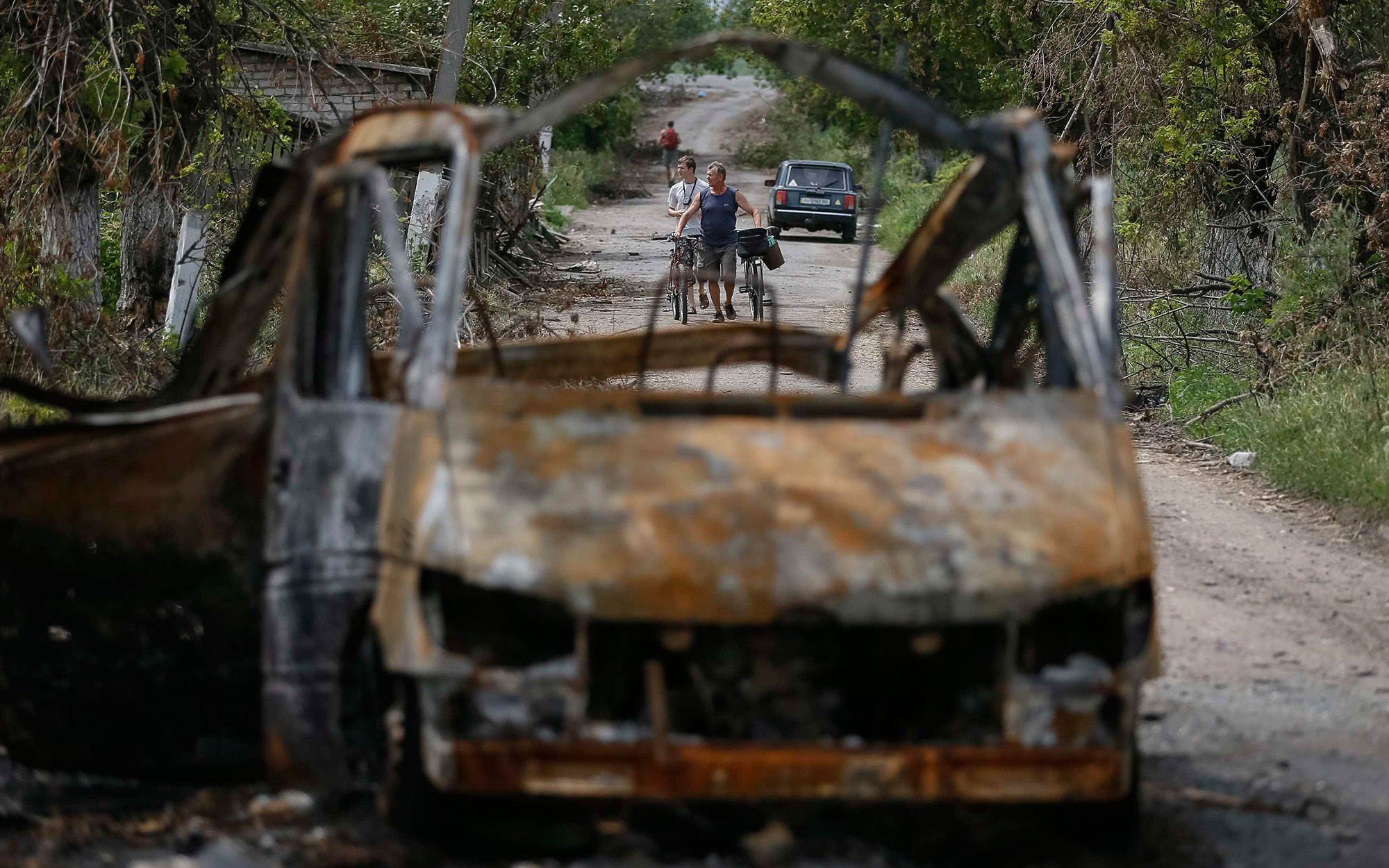 Местные жители возле автомобиля, повреждённого недавним обстрелом, в деревне Семёновка 13 июля 2014 года.Фото: © REUTERS/Gleb Garanich