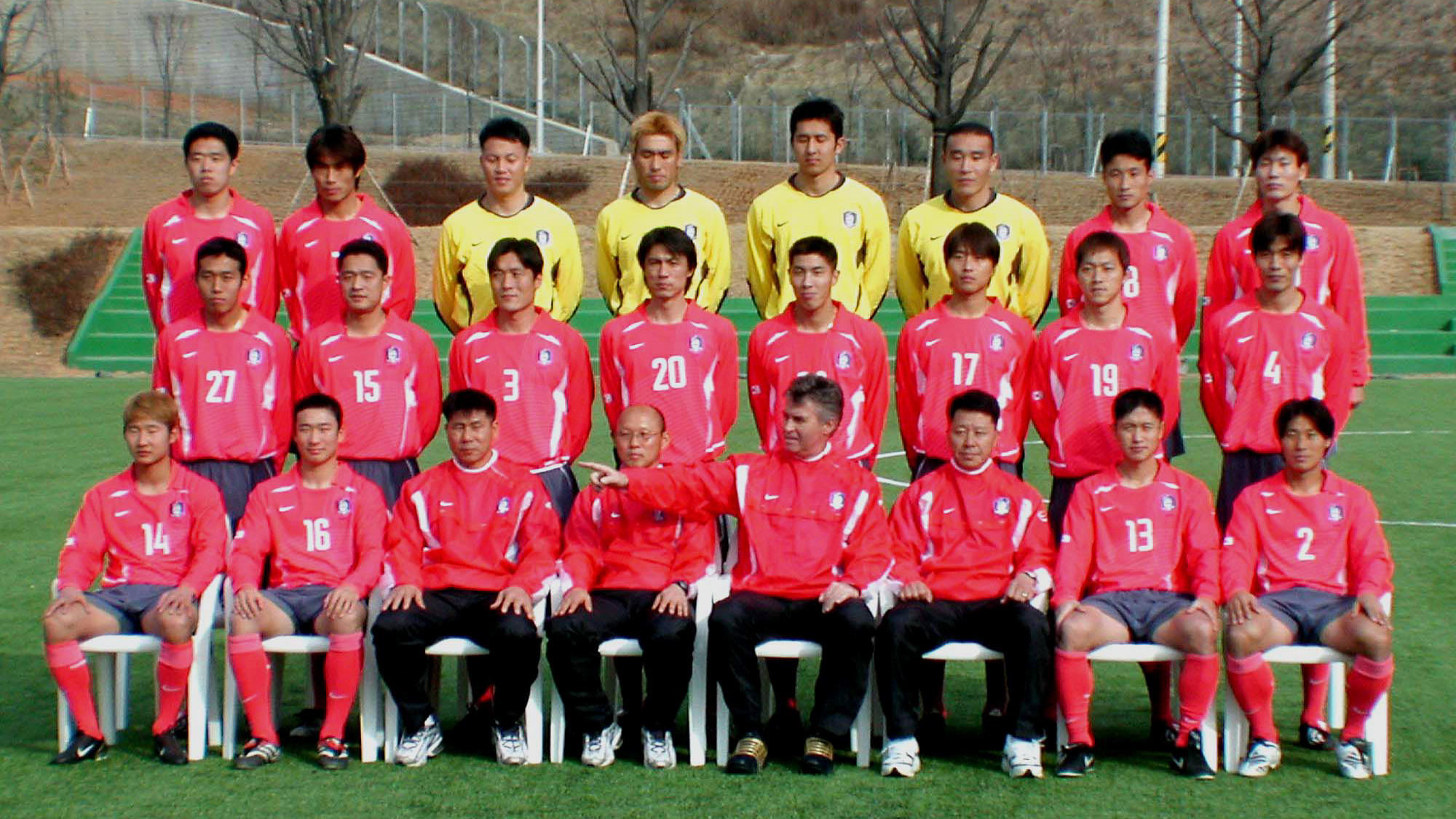 Главный тренер южнокорейской национальной футбольной команды Гус Хиддинк, четвёртый справа на линии фронта, и его игроки позируют фотографам в новой униформе на церемонии открытия чемпионата мира по футболу 2002 года в Корее/Японии в тренировочном центре в Паджу к северу от Сеула, 4 марта 2002 года. Фото: © AP Photo/Yun Jai-hyoung