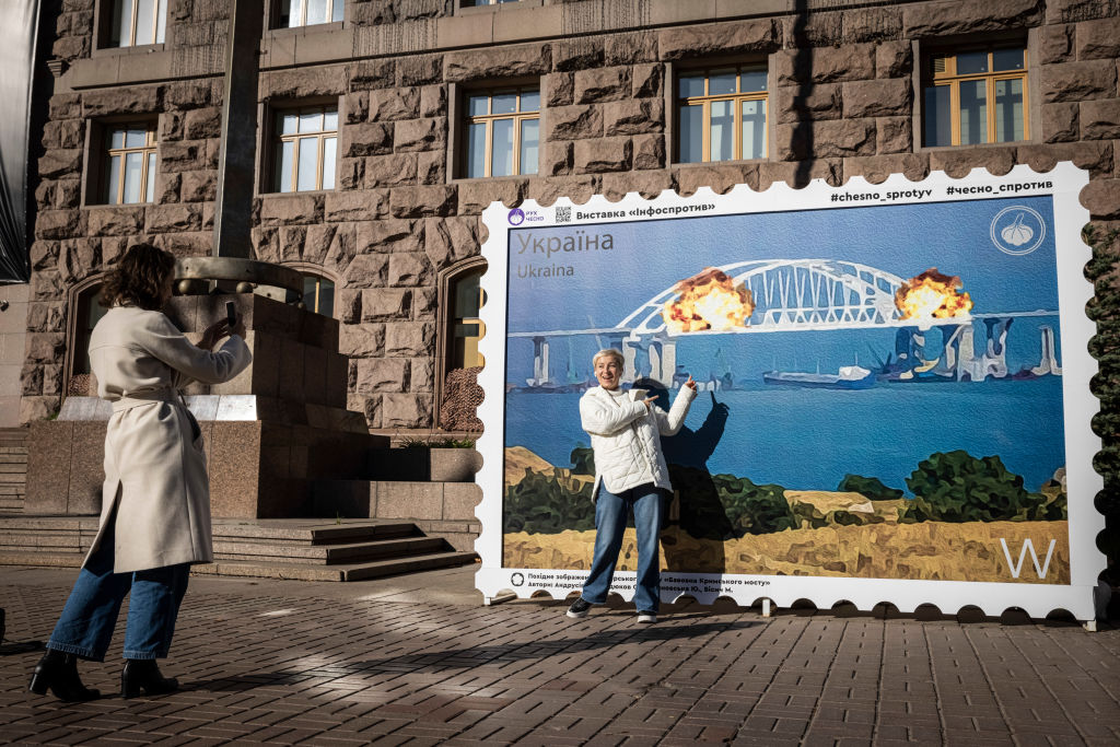 Люди позируют перед изображением почтовой марки, на которой изображён горящий Керченский мост, 8 октября 2022 года в центре Киева, Украина. Фото © Getty Images / Ed Ram