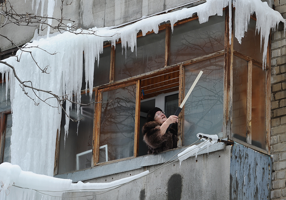 Женщина сбивает сосульки и наледь на балконе жилого дома. Фото © ТАСС / Александр Рюмин