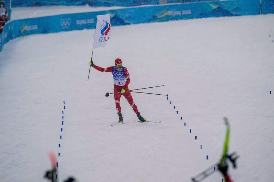 Сергей Устюгов финиширует с флагом ОКР в лыжной эстафете. Фото © Beijing2022.cn / Michel Cottin/Agence Zoom / Getty Images