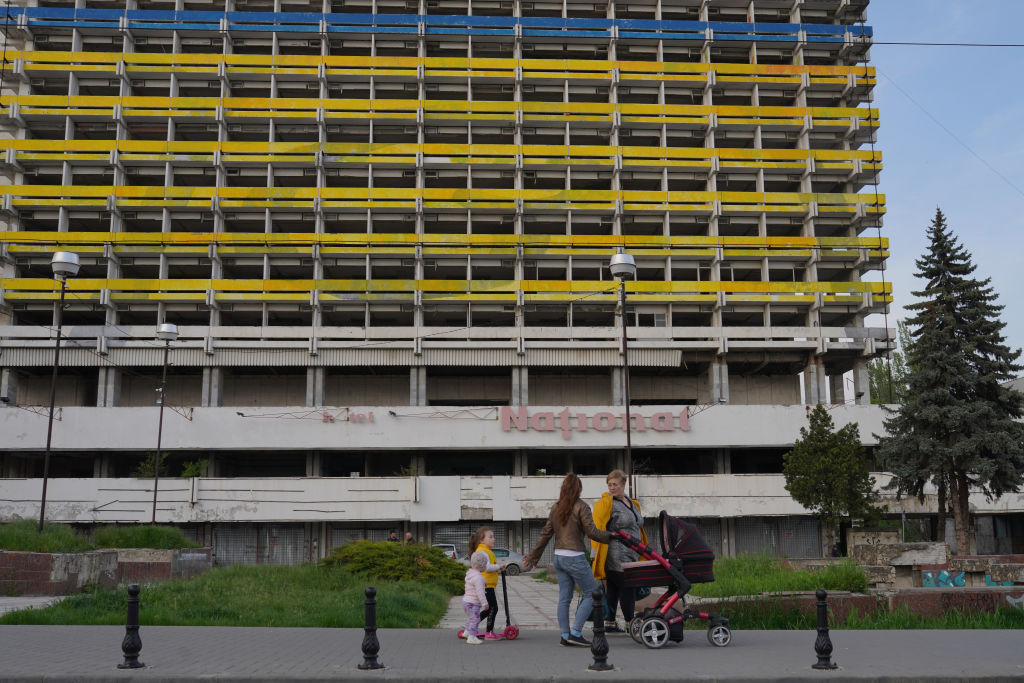Семья проходит мимо бывшей советской гостиницы "Националь", ныне заброшенной и окрашенной в цвета украинского флага, 3 мая 2022 года, Кишинёв, Молдова
