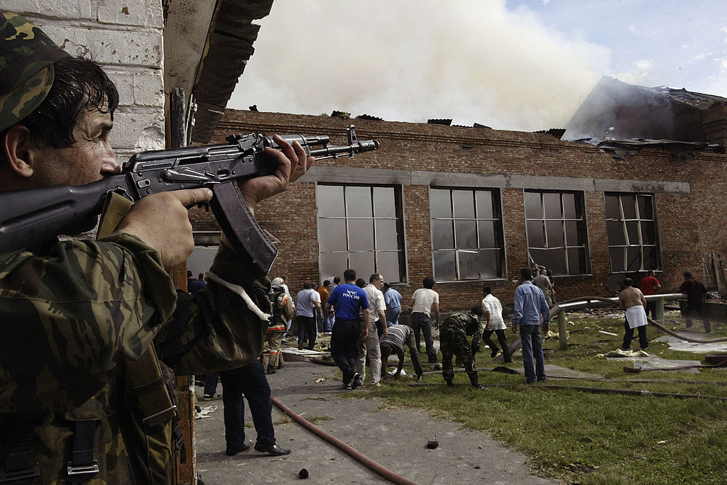 Солдат закрывает крышу, пока волонтёры осматривают территорию после штурма спецназом школы, захваченной чеченскими сепаратистами 3 сентября 2004 года в городе Беслане, Россия. Фото © Getty Images / Oleg Nikishin