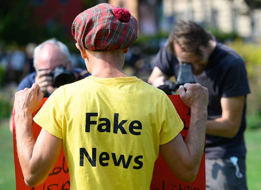 Мужчина в "футболке с фейковыми новостями" стоит перед двумя представителями прессы на митинге. Фото © Getty Images / picture alliance
